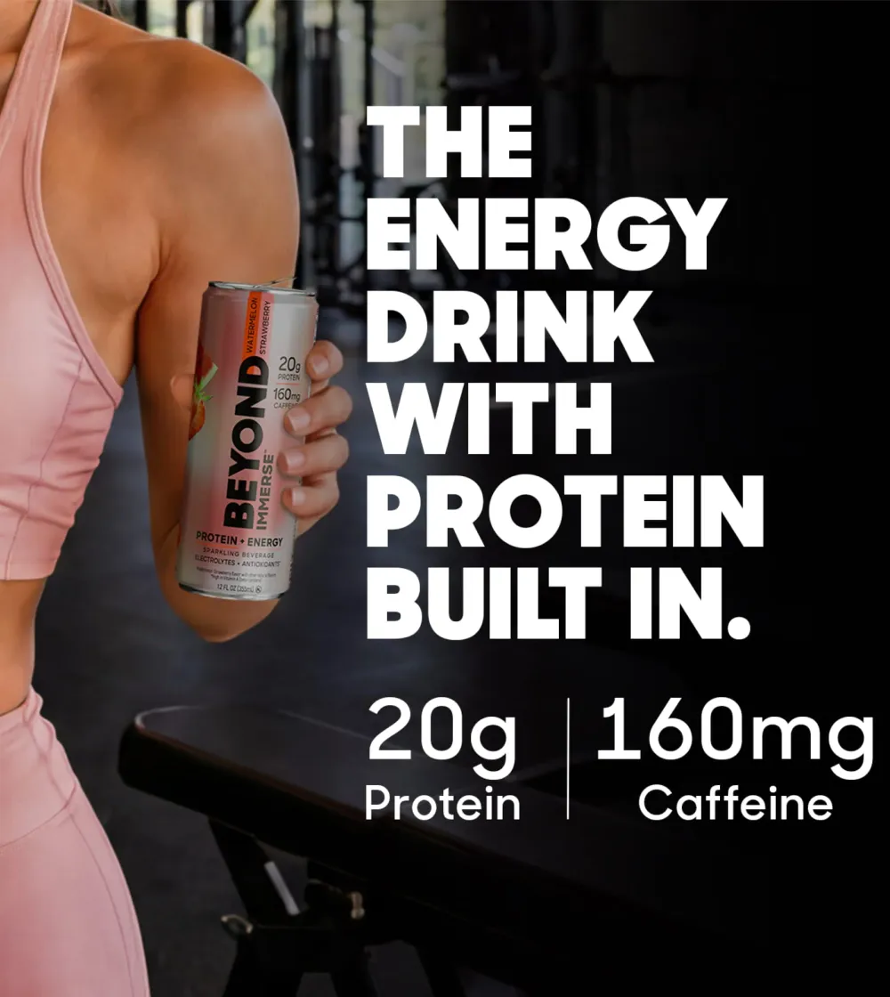 A person in pink athletic clothing holds a slim can labeled “BEYOND IMMERSE” in a dark gym setting