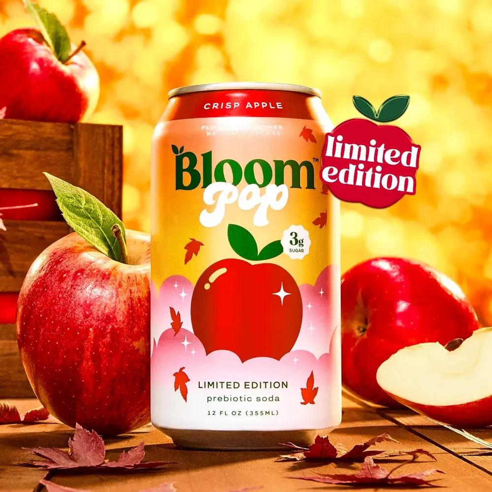 Limited-edition Bloom Pop Crisp Apple can surrounded by red apples, a wooden crate and autumn leaves