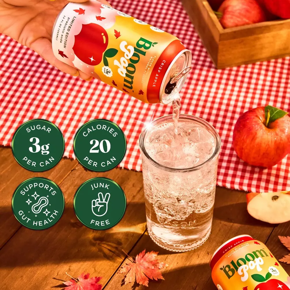 Bloom Pop Crisp Apple poured over ice on a checked tablecloth, with callouts for 3g sugar and 20 calories per can