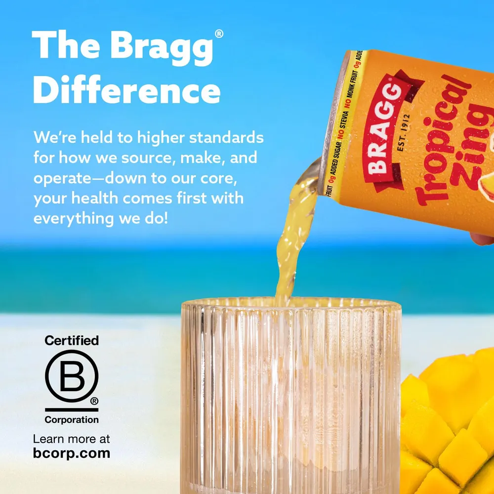A Bragg Tropical Zing Mango Pineapple can pours a golden sparkling drink into a ribbed glass on a beach, next to cut mango