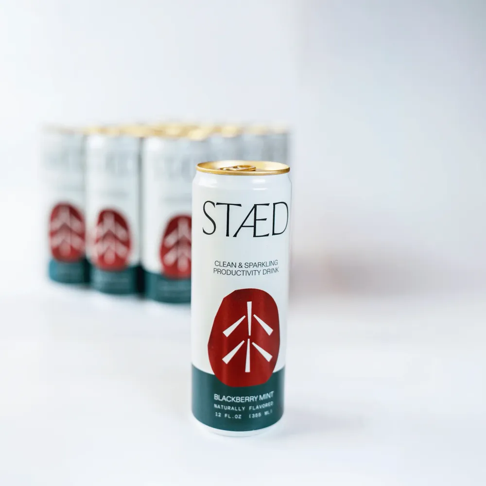 A white-and-dark-teal Staed Clean & Sparkling Productivity Drink can stands in the foreground, with several matching cans blurred behind it