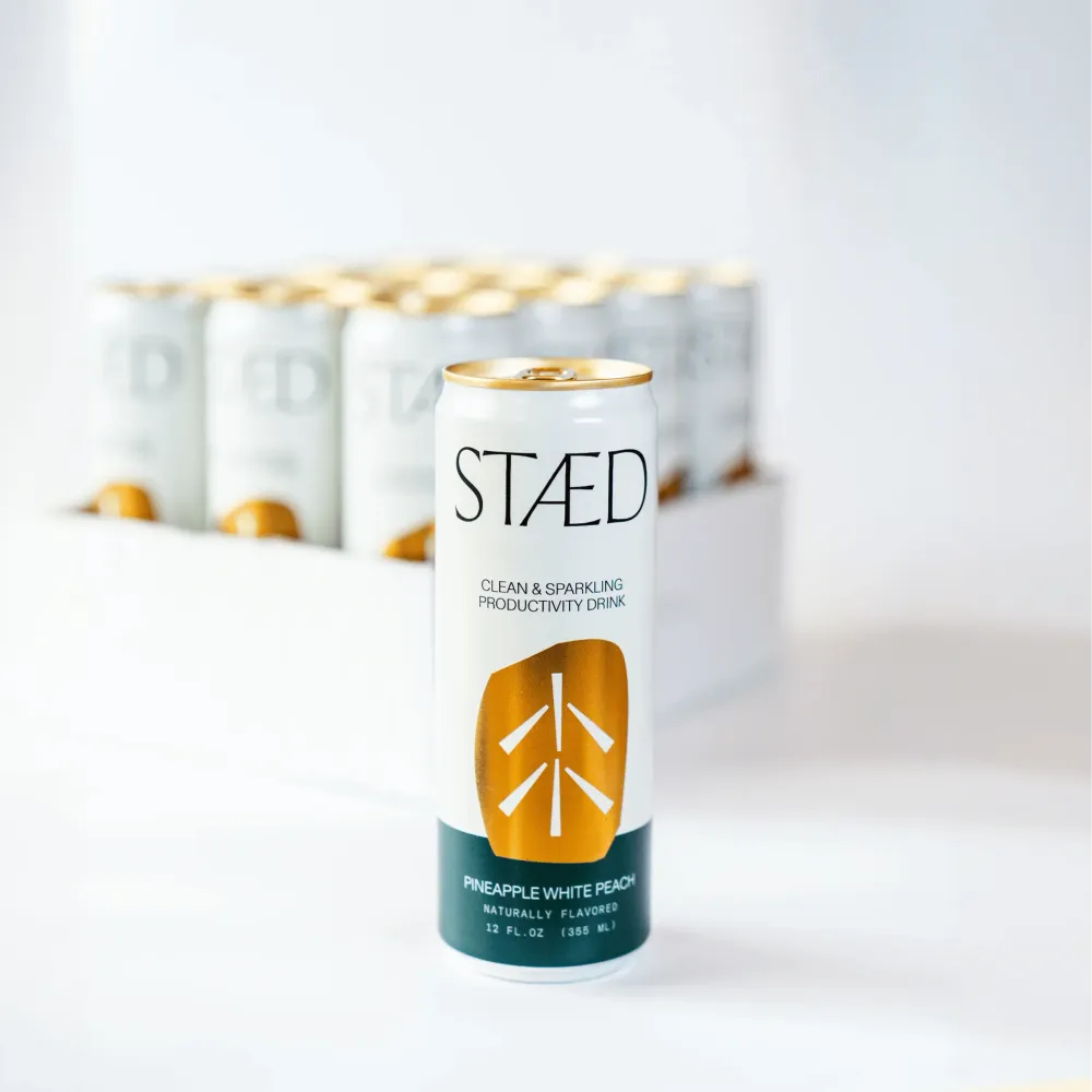 A white Staed Clean & Sparkling Productivity Drink can stands in front of a blurred row of matching cans on a bright white surface